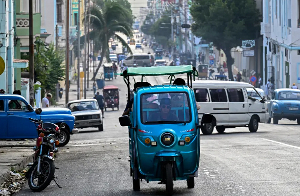 People ride an electric tricycle along a street in Havana, Cuba