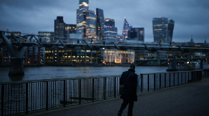 Man walks along South Bank, London, with financial district high-rises in background