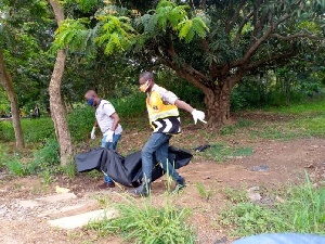 Corpse draped in black body bag being carried in