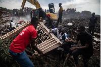 Men fight over a metallic door from the debris of a house hit by a landfill collapse in Kampala