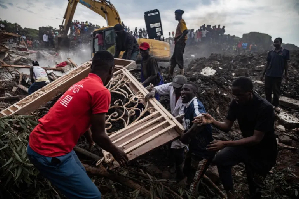 Men fight over a metallic door from the debris of a house hit by a landfill collapse in Kampala