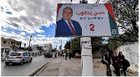 Women walk underneath an electoral billboard for a candidate running in the Tunisian elections
