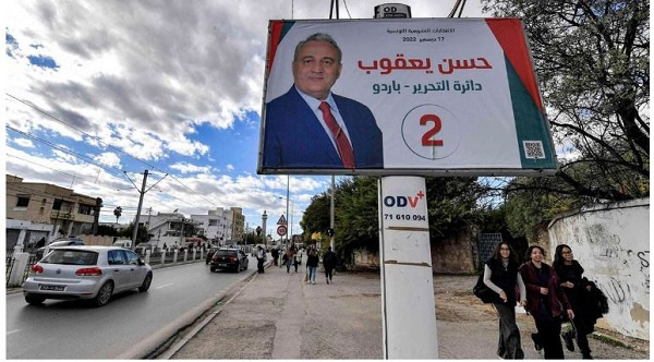 Women walk underneath an electoral billboard for a candidate running in the Tunisian elections