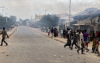 Civilians gather as smoke billows from a shop hit by artillery following clashes
