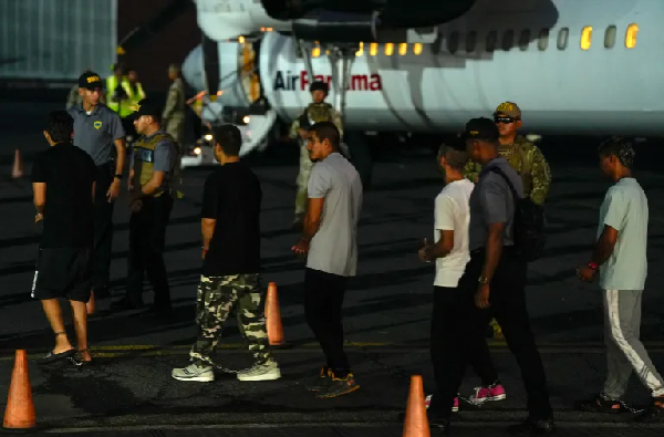 Colombian migrants, with their hands and feet handcuffed, line up to climb a plane