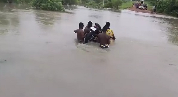 Men carrying a motorcycle across a flooded road