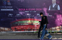 People walk past a hoarding of AI Expo along a street on the eve of the India AI Impact Summit 2026