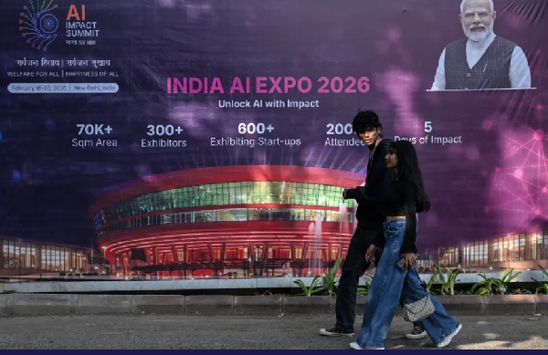 People walk past a hoarding of AI Expo along a street on the eve of the India AI Impact Summit 2026