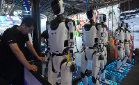 A worker near a line of humanoid robots displayed at the World AI Conference in Shanghai on July 17