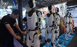 A worker near a line of humanoid robots displayed at the World AI Conference in Shanghai on July 17