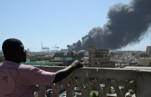 A man watches as smoke billows after a drone attack on Port Sudan