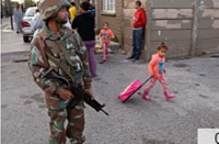 A South African soldier provide security for policemen as they look for drugs, with a child