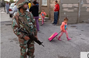 A South African soldier provide security for policemen as they look for drugs, with a child