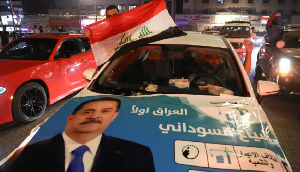 Man holds an Iraqi flag with an election poster featuring incumbent PM Mohammed Shia al-Sudani