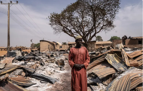 A resident stands among burned debris and damaged homes after a deadly attack on Woro, Kwara State