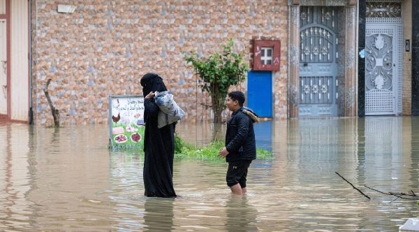 A mother and her son evacuate through a flooded street road after heavy rainfall in Ksar El Kebir