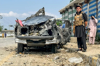 A security person stands guard beside the wreckage of a vehicle after a blast in Bajaur