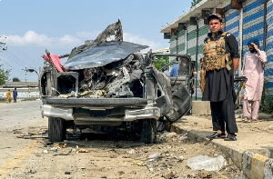 A security person stands guard beside the wreckage of a vehicle after a blast in Bajaur