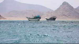A floating dredging platform and commercial vessels lie anchored amid haze in the Strait of Hormuz