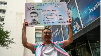 Activist Henry Tse holds up a mock ID card outside the immigration tower in Hong Kong after receivin