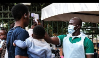 A health official uses a thermometer to screen people in front of Kibuli Muslim Hospital in Kampala,