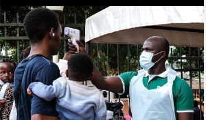 A health official uses a thermometer to screen people in front of Kibuli Muslim Hospital in Kampala,