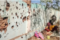 Displaced Sudanese sit next to a bullet-riddled wall, taking shelter in a school