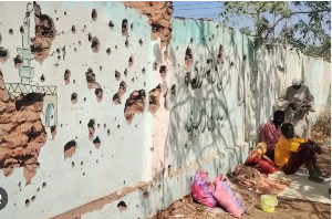 Displaced Sudanese sit next to a bullet-riddled wall, taking shelter in a school