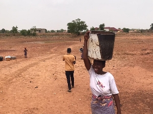 A resident after hours of collecting water at a dried up dam in Tamale