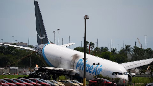 An Amazon cargo plane lies damaged near a parking lot two days after overshooting a runway