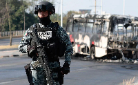 A member of Mexico's National Guard stands near a of bus that appears to have been set on fire