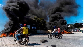 Motorcyclists drive by burning tires during a police demonstration after a gang attack on a police