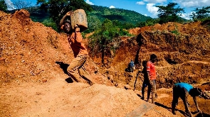 A miner carries a load of ore at Manzou Farm in Mazowe, Zimbabwe on April 5, 2018