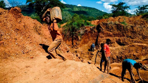 A miner carries a load of ore at Manzou Farm in Mazowe, Zimbabwe on April 5, 2018