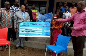 Rev. Erasmus Mensah Laryea presenting the cheque and the chairs to the headmistress of the school