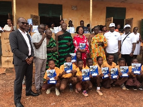 Officials of BOST, and some basic pupils displaying the exercise books received from the donation
