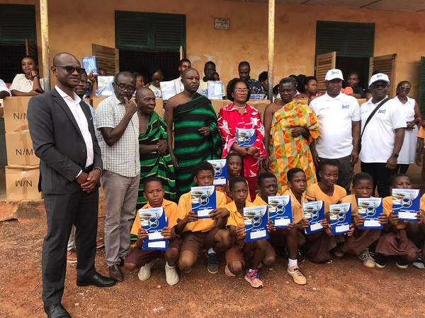 Officials of BOST, and some basic pupils displaying the exercise books received from the donation