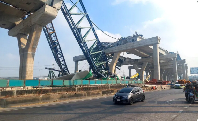 Cars drive next to a collapsed crane that crushed two vehicles during construction