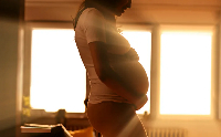Pregnant woman standing in front of brightly backlit window