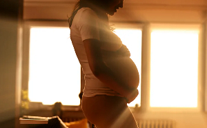 Pregnant woman standing in front of brightly backlit window