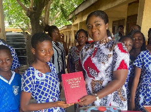 Akosua Manu presents a copy of donated books to a pupil