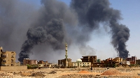 A man walks while smoke rises above buildings after aerial bombardment in Khartoum North, Sudan
