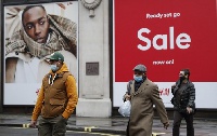 People wearing face masks walk past sale advertisement on Oxford Street in London, Britain