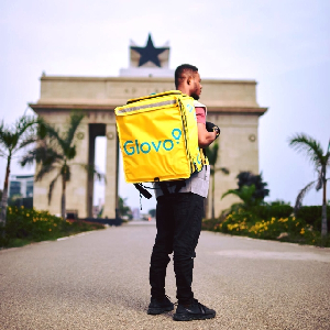 Man with Glovo-branded bag and in the background is the iconic Independence Arch