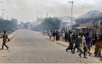 Civilians gather as smoke billows from a shop hit by artillery following clashes