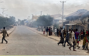 Civilians gather as smoke billows from a shop hit by artillery following clashes