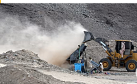 A front-loader deposits dirt and crushed rock into a processing machine