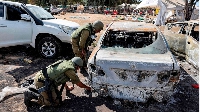 Soldiers search the remains of a torched vehicle for forensic evidence