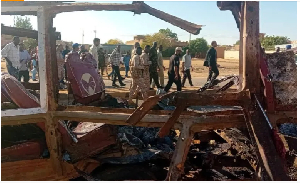 People walk past a destroyed vehicle after shelling by the Rapid Support Forces in Omdurman, Sudan