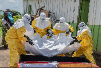 Red Cross workers carry the body of a person who died of Ebola into a coffin at a health center
